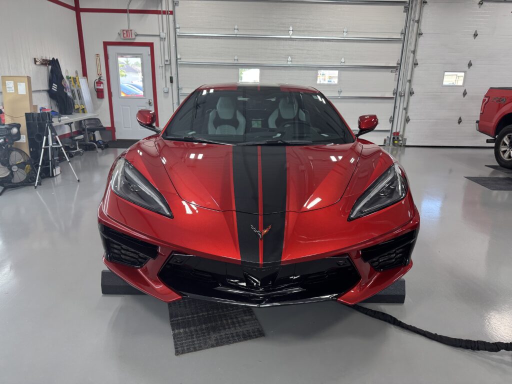 Front view of a red Corvette with black racing stripes inside SS Auto Detailing shop after ceramic window tint installation in St. Henry, Ohio.